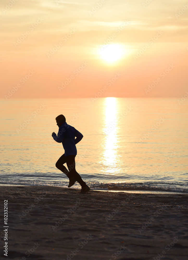 silhouette young sport man running outdoors on beach at sunset with orange sky