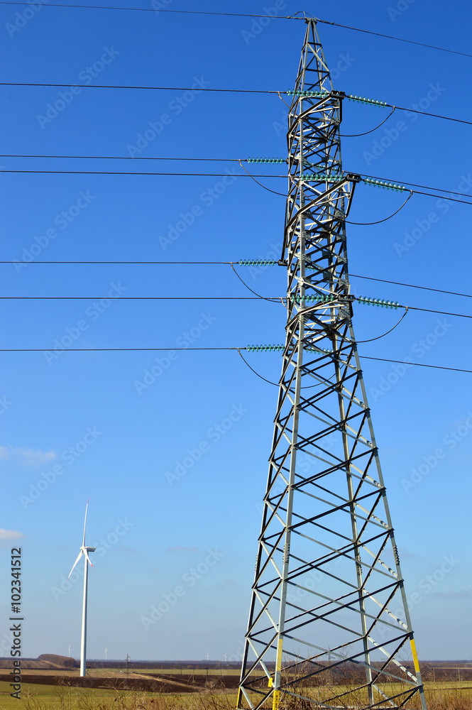 Tall electric pole, wind generator seen in the distance Tall electric pole, wind generator seen in the distance