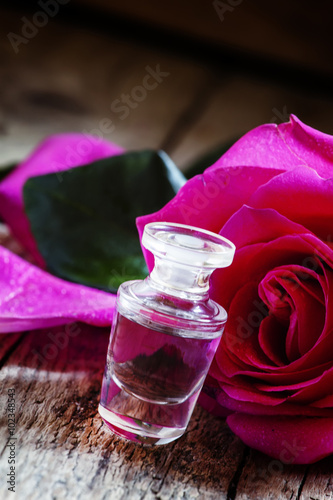 Rose essential oil in a small bottle and pink rose with drops on