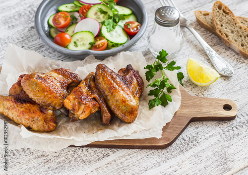 Spicy chicken wings and fresh vegetable salad on wooden white background