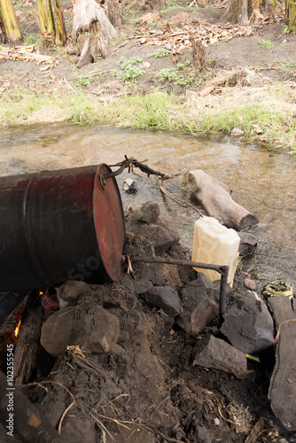 makeshift apparature on river to distill uganda waragi gin (moonshine) from bananas photo