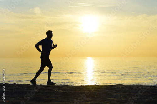 silhouette young sport man running outdoors on beach at sunset with orange sky