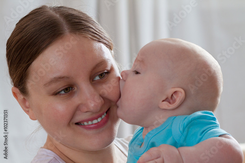 Funny baby boy kissing his mother indoors