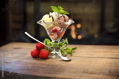 Delicious ice cream dessert with strawberries and peppermint on a wooden table photo