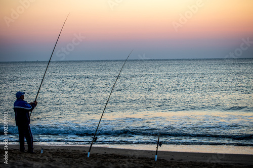 Angler im pastellfarbenen Sonnenaufgang am Meer