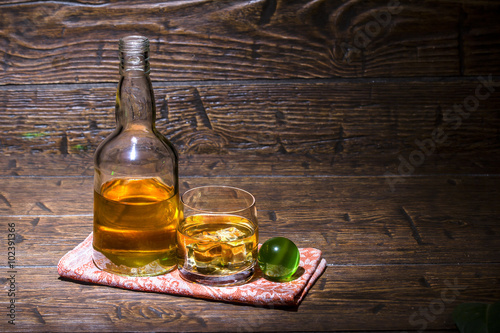 Bottle with a glass whiskey and green ball with laser ray