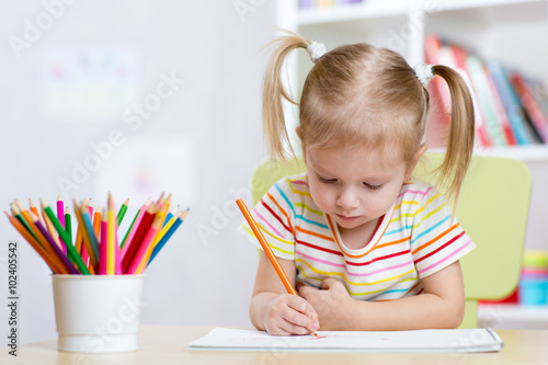 Child girl drawing with colorful pencils in nursery photo