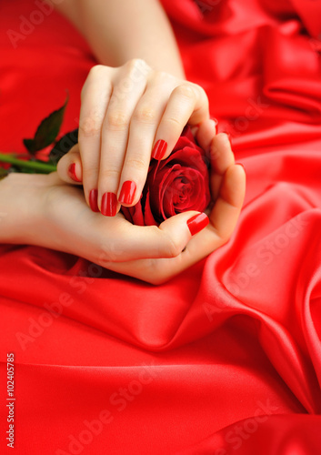 Red Rose in female hands on a background of red silk