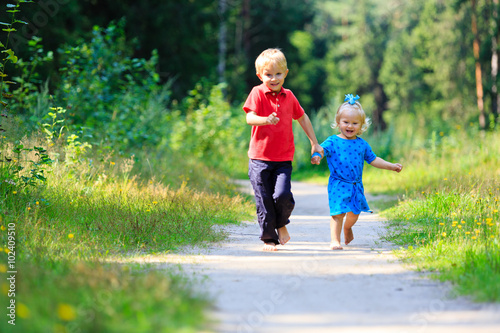 little boy and toddler girl running in summer forest