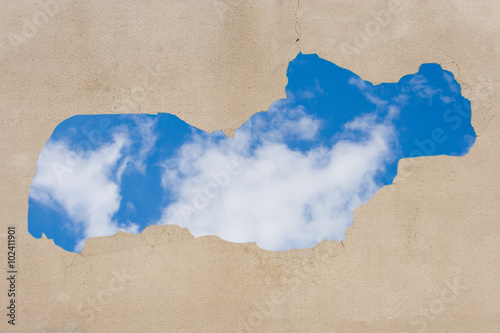 Gray wall with peeling plaster (with blue sky and clouds showing through the hole)