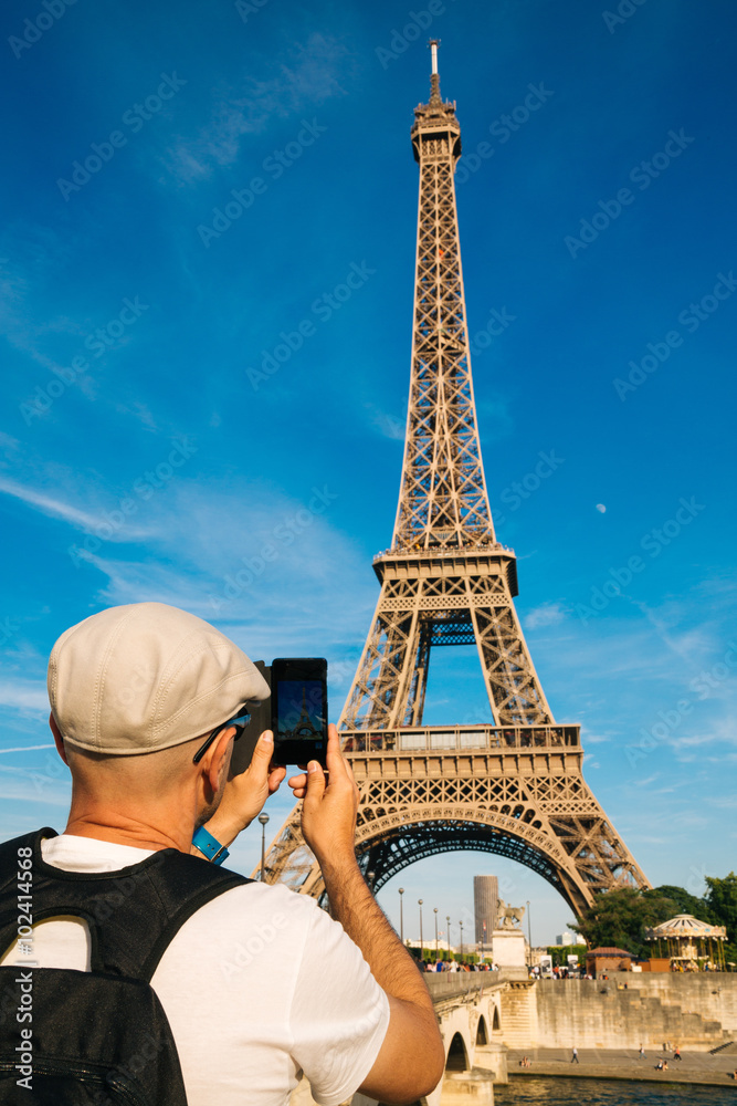 Tourist man taking pictures of the Eiffel Tower with a smart phone