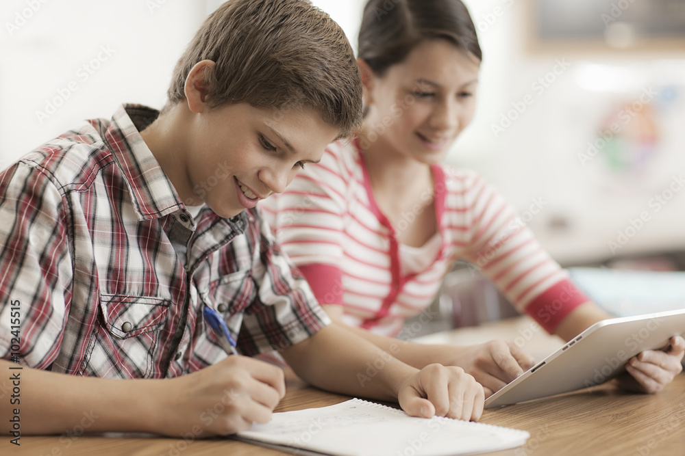 Two children, a boy and girl sitting in class, sharing a digital tablet. Two children, a boy and girl sitting in class, sharing a digital tablet.