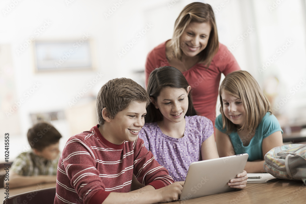 A group of students in class and an adult teacher looking at a digital tablet. A group of students in class and an adult teacher looking at a digital tablet.