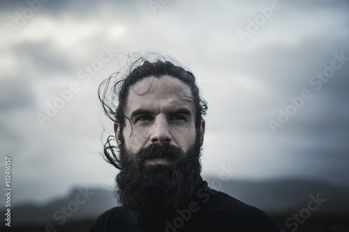 Man with black hair and beard and standing outdoors photo
