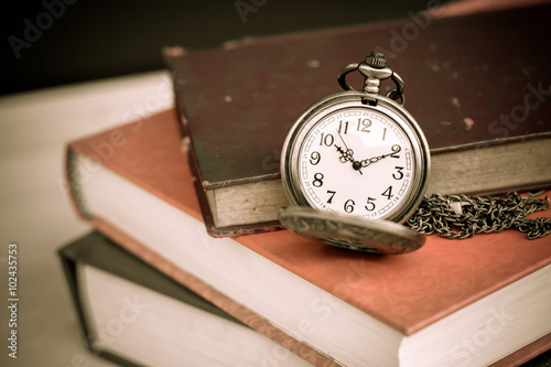 Old vintage books and pocket watches on wooden desk. Retro style filtered photo