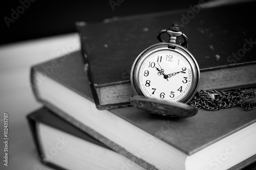 Old vintage books and pocket watches on wooden desk. Black and white style filtered photo