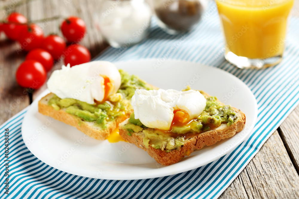 Poached eggs with avocado on toasts on grey wooden table
