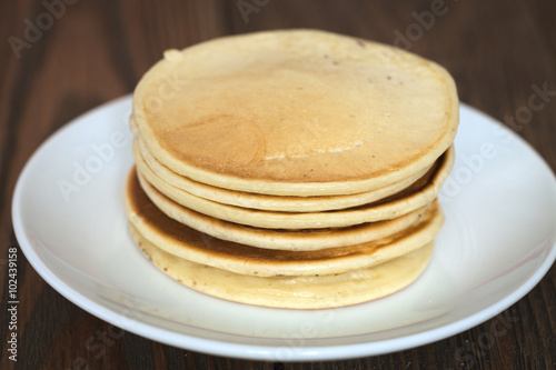 stack of pancakes on a white plate, brown background of wooden p