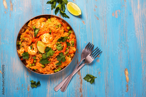 Traditional spanish paella dish with seafood, peas, rice and chicken over grunge blue background. Top view. Selective focus