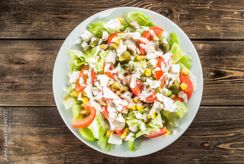 Salad with vegetables, olives and sauce on wooden background.