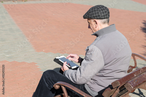 Senior elderly man using tablet computer sitting on bench