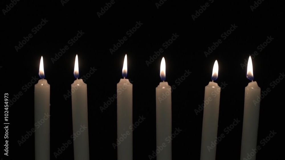 Six candles are placed in a row with flames on dark background. Six candles are placed in a row with flames on dark background.