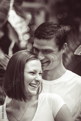 Black and white close-up portrait of two people couple, Caucasian man woman girl together, standing in park outside, smiling laughing hugging, looking away, intimate moment of love, Valentines day