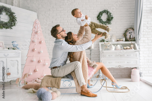 Young happy family holding baby in christmas decor studio