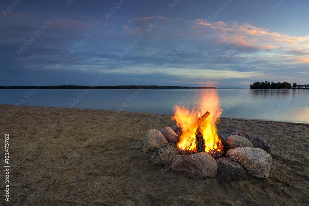 Fototapeta premium Camp fire on sandy beach, beside lake at sunset. Minnesota, USA