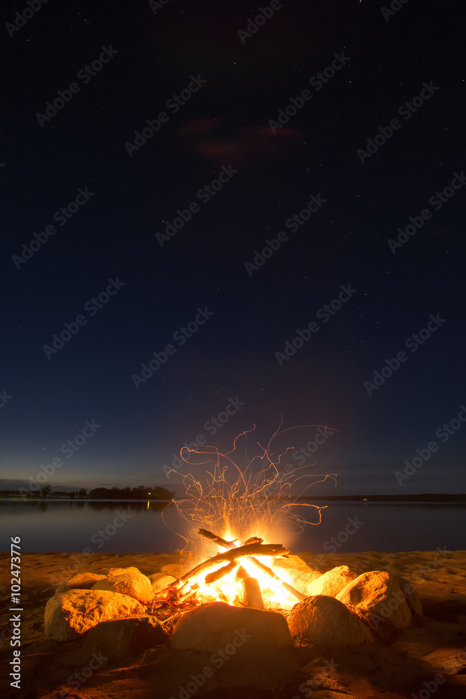 Naklejka premium Sparking camp fire beside lake under a starry sky