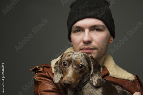 Best friends/Handsome young man wearing leather jacket & black watch cap holding small dapple dachshund