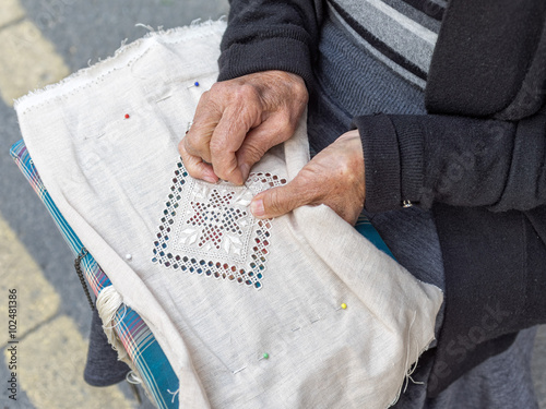 Woman lace-maker sits with needlework on knees and embroiders. Pano Lefkara, Cyprus.
