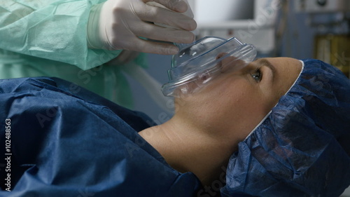 Young adult female patient falls asleep after taking a breath into the anesthesia mask at the operating room