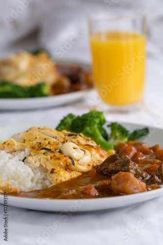 Japanese curry, a colourful dish of Japanese curry rice with omelette and broccoli with a glass of orange juice.