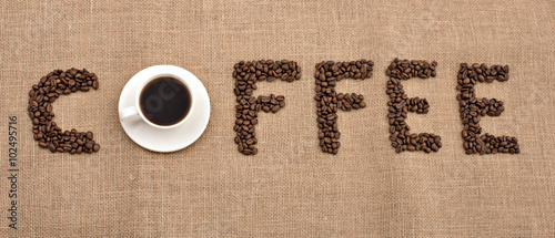 word coffee of coffee beans and cup of black coffee on bagging background