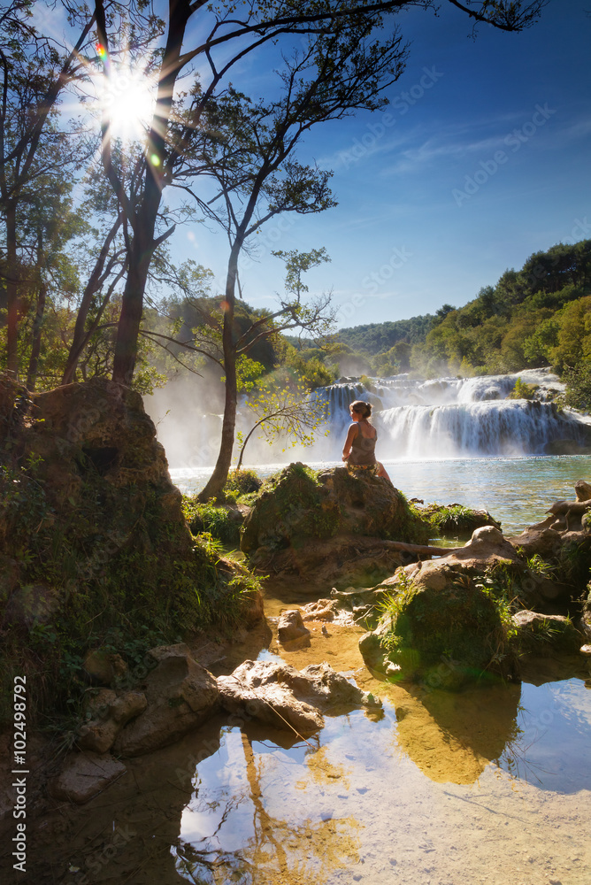 Fototapeta premium Beautiful woman sits at the waterfall in Krka national park, Croatia