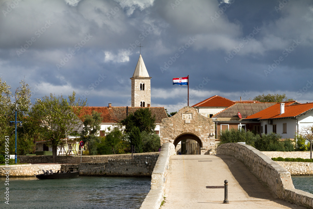 Bridge leading to a small town in croatia with the croatian flag waving in the wind