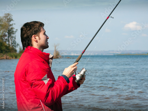fisherman in a red jacket throws a spinning bait from the shore of the river