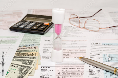 Hourglass with tax form 1040, calculator, pen and dollar bills