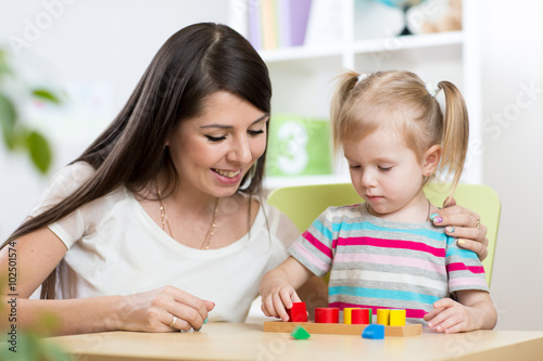 Little girl is solving puzzle. Mother watching at her actions