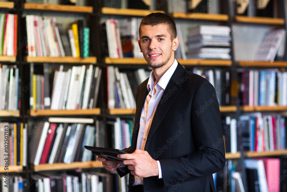 student using a tablet in the library. student stands with tablet in his hands in a library student using a tablet in the library. student stands with tablet in his hands in a library