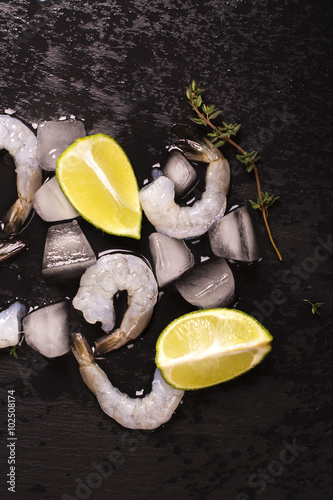 Raw prawns with lime and thyme over black wet stone background. Toned image. Selective focus