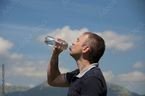 A man drinks water from a bottle in the mountains