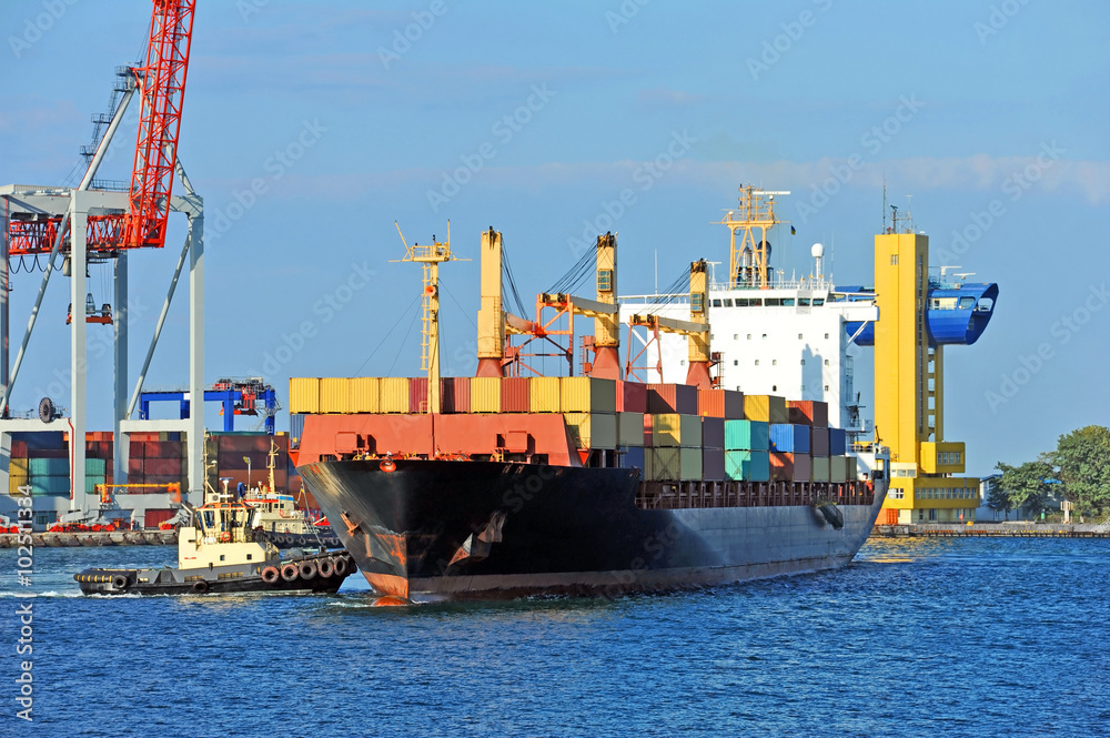Fototapeta premium Tugboat assisting container cargo ship to harbor quayside