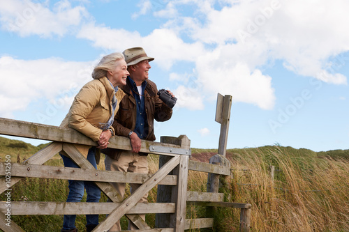 Senior Couple With Binoculars Walking In Countryside