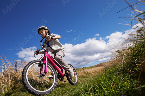 Fototapeta Naklejka Na Ścianę i Meble -  Low Angle Shot Of Boy Riding Bike Through Countryside