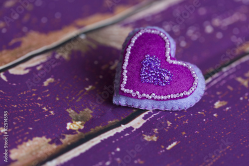 Сердечко из сиреневого/фиолетового фетра ручной работы, вышитое бисером, на старом/вытертом  деревянном полу 