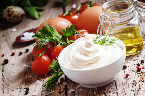 Homemade mayonnaise sauce in a white bowl, jar with olive oil, e