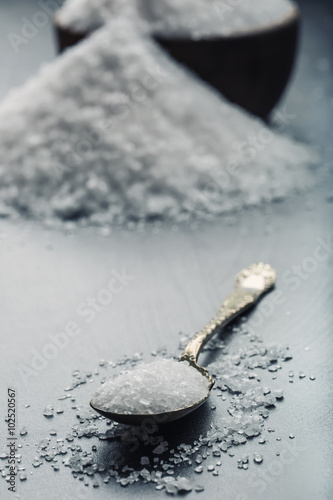 Salt. Coarse grained sea salt on granite - concrete stone background with vintage spoon and wooden bowl.