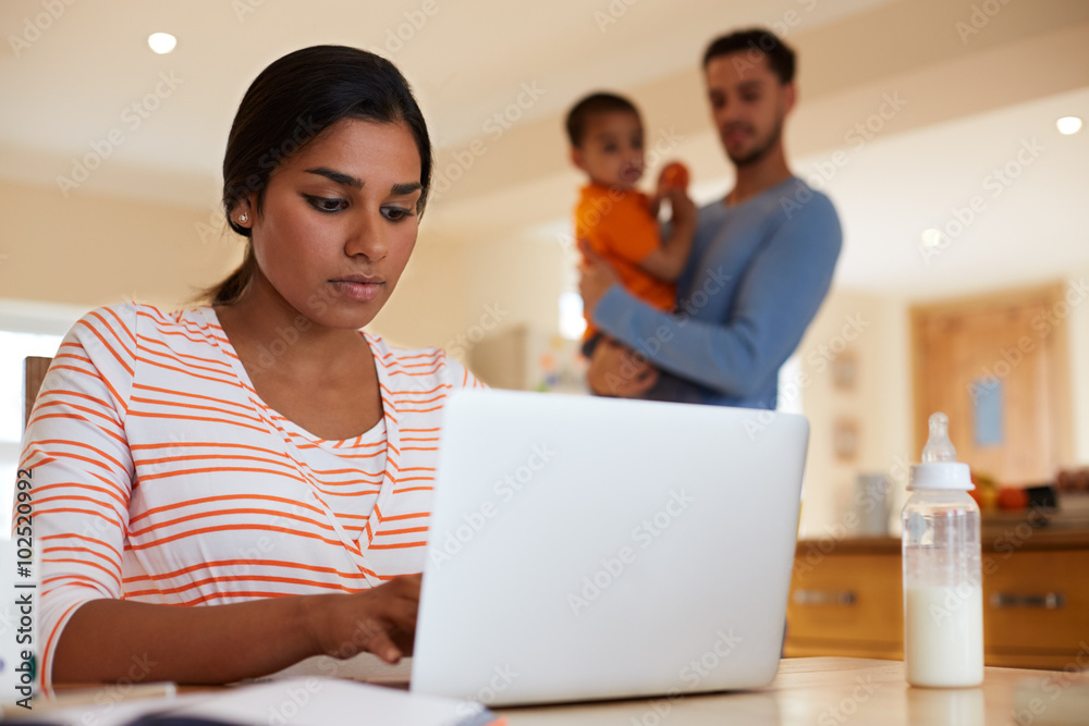 Family In Kitchen With Mother Using Laptop At Table